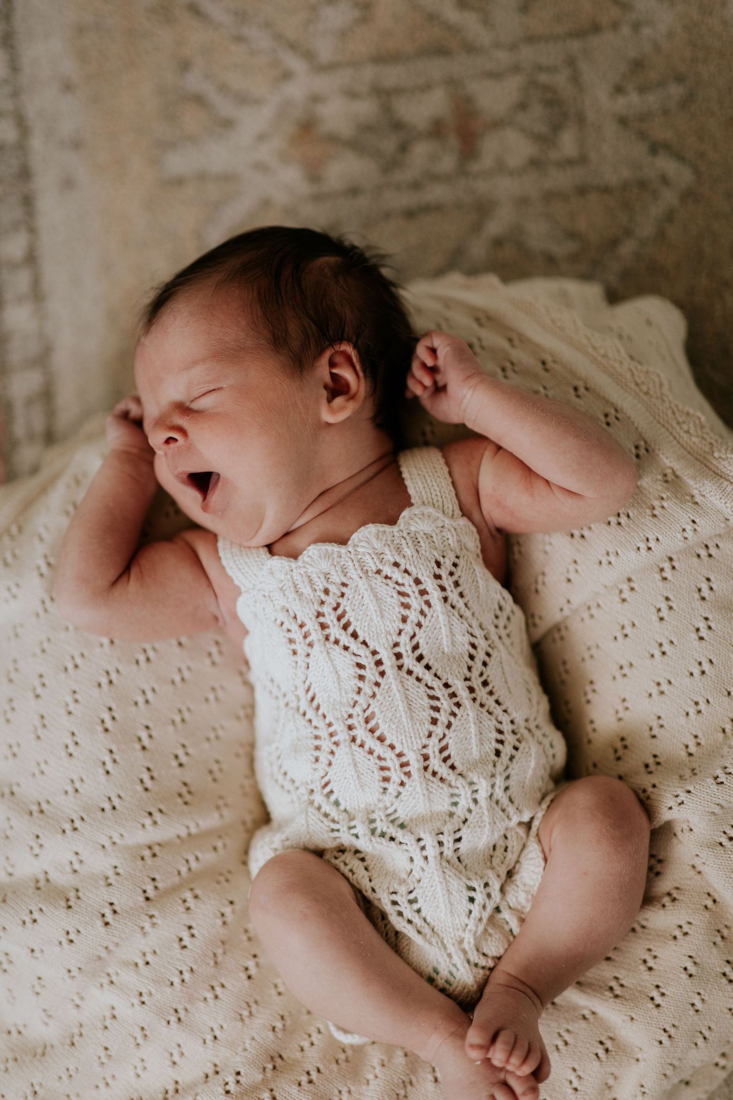 Sleeping newborn in white knit romper on textured cream blanket.