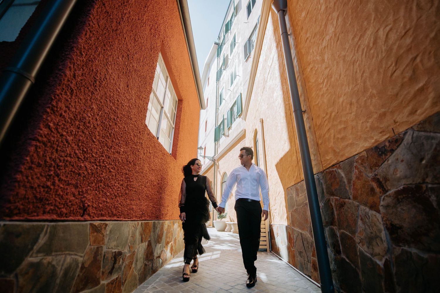 Couple walking hand in hand through narrow colorful European alleyway.