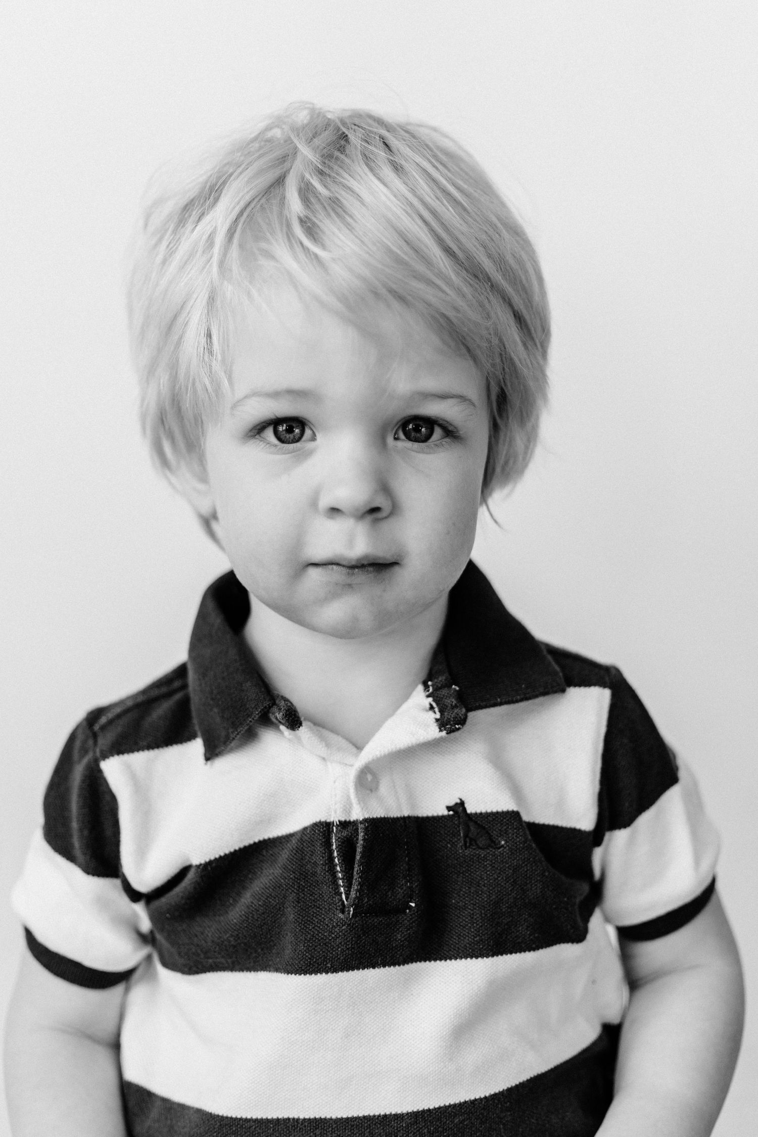 Black and white portrait of a young child wearing a striped polo shirt against a plain background.