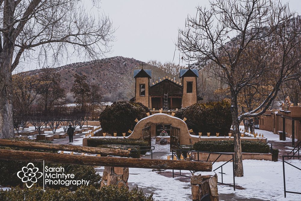 Snow-covered adobe church with twin bell towers on winter morning.