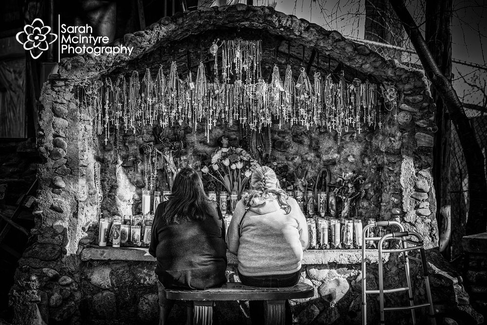 Rustic shrine with religious artifacts and candles in black and white.