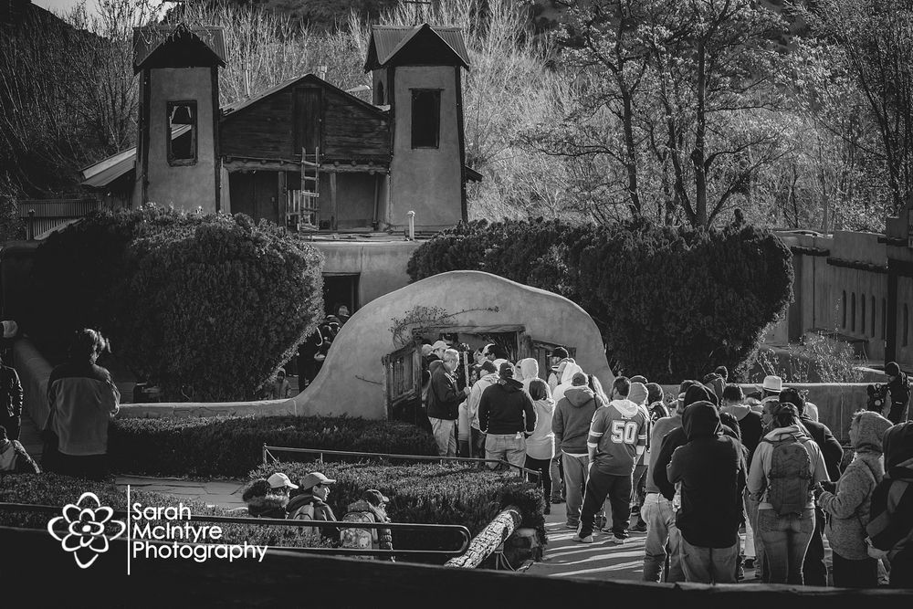 Visitors gather outside historic adobe church during a community event in black and white.