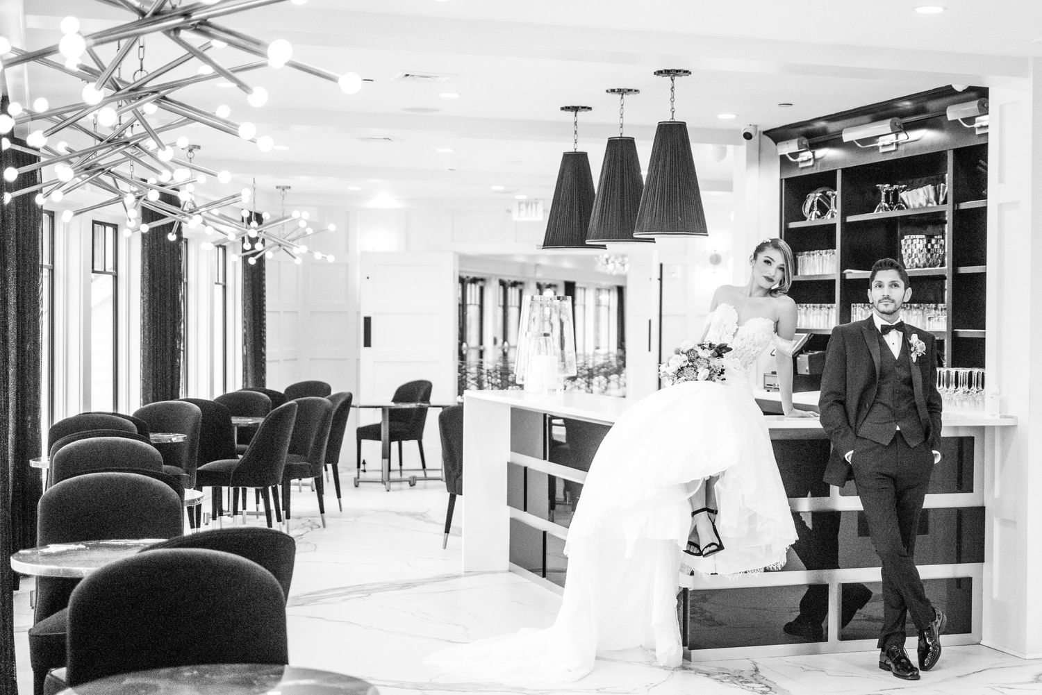 The bride seated at the bar of Waters Edge, with the groom leaning against the bar beside her.