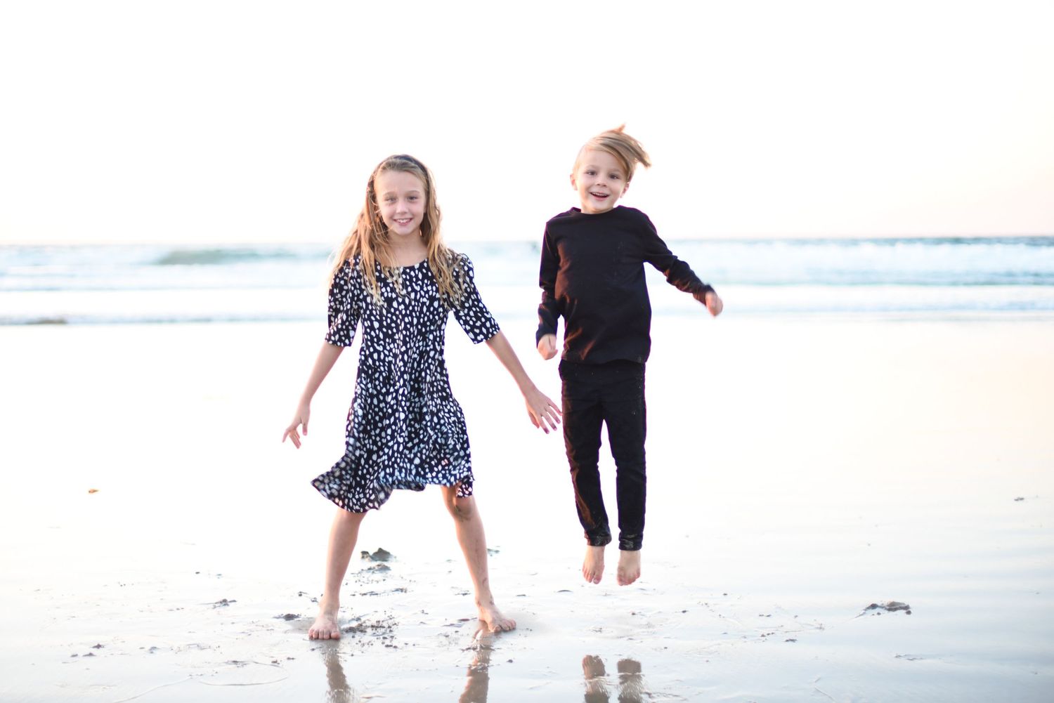 A couple walks playfully together on a sunny beach with waves crashing in the background.