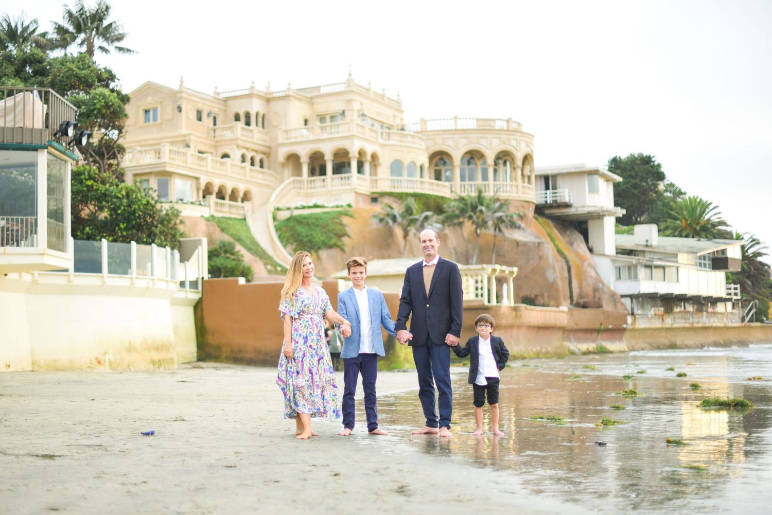Family walking and enjoying time together along a beachfront with buildings in background.