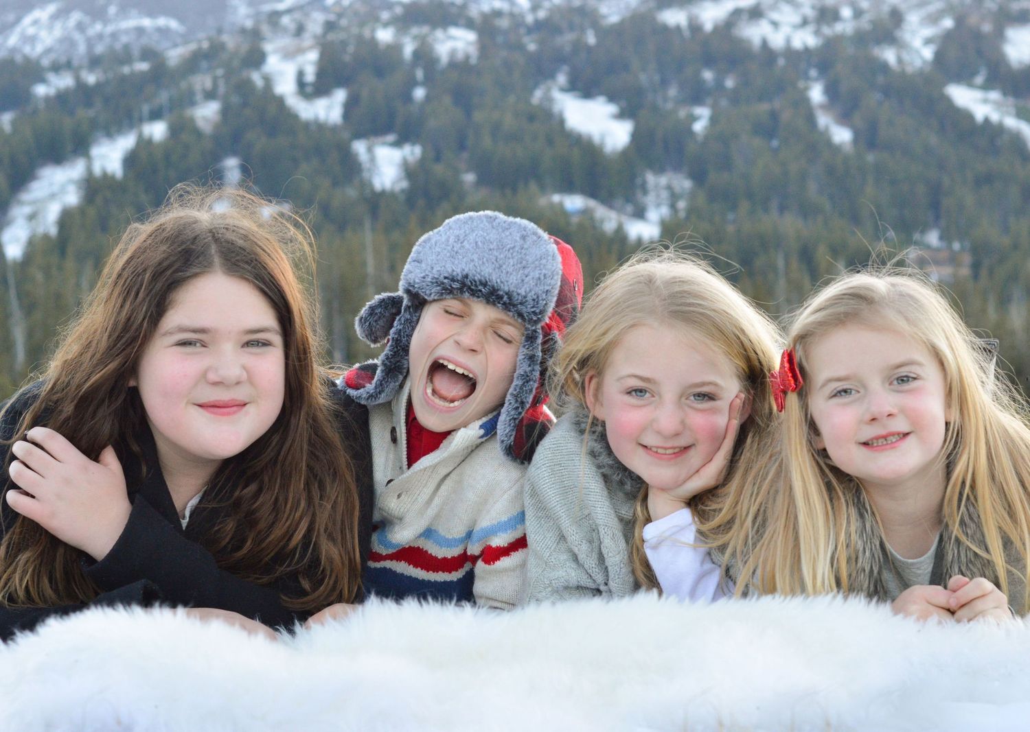 A group poses for winter photos in the snow with a mountain ski resort backdrop in the background.