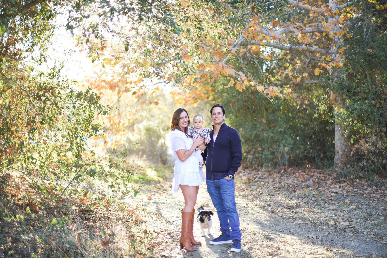 Couple walking through a wooded area with dappled sunlight filtering through the trees.