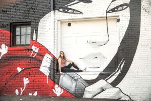 Urban portrait near large-scale street art mural featuring monochromatic face design.