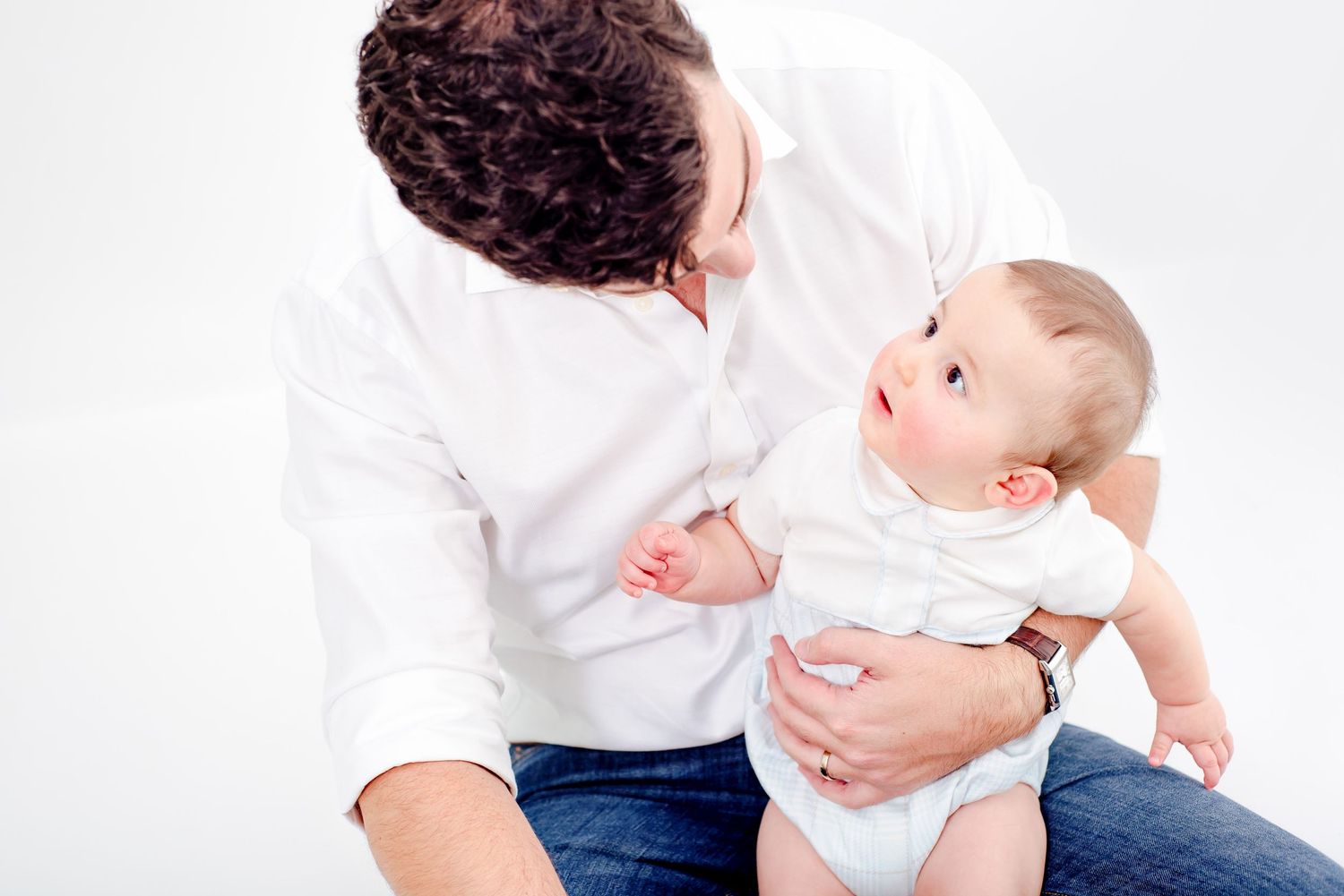 Parent and baby share intimate moment during lifestyle photography session on white backdrop.