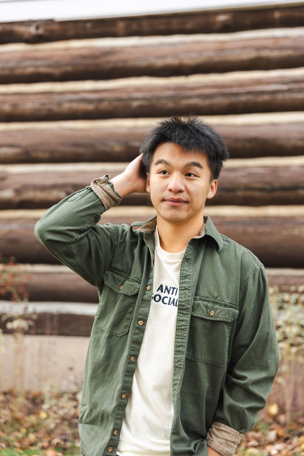 Person in olive green jacket poses playfully against rustic wooden wall background.