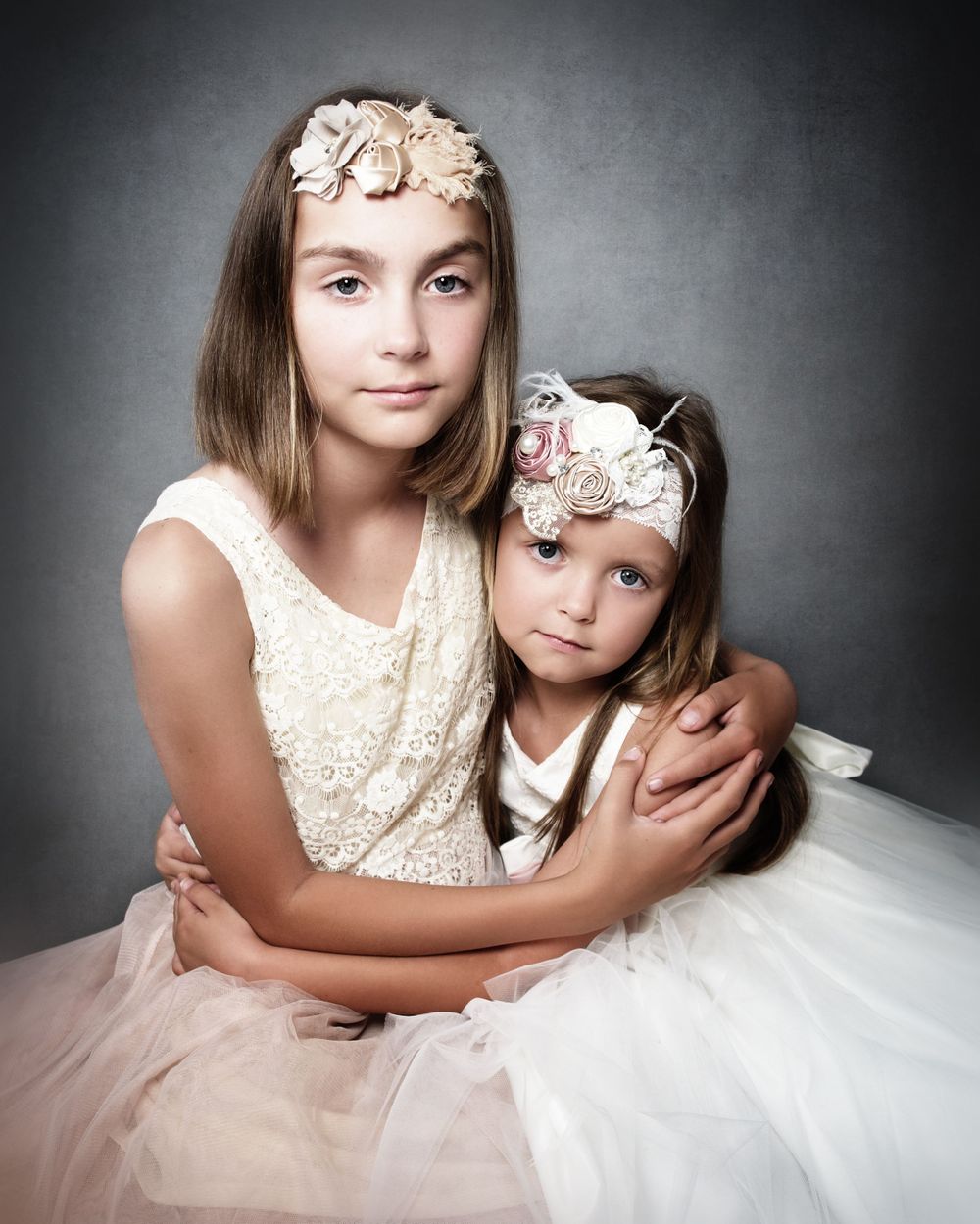 portrait of two sisters holding each other wearing peach and white dresses and headband