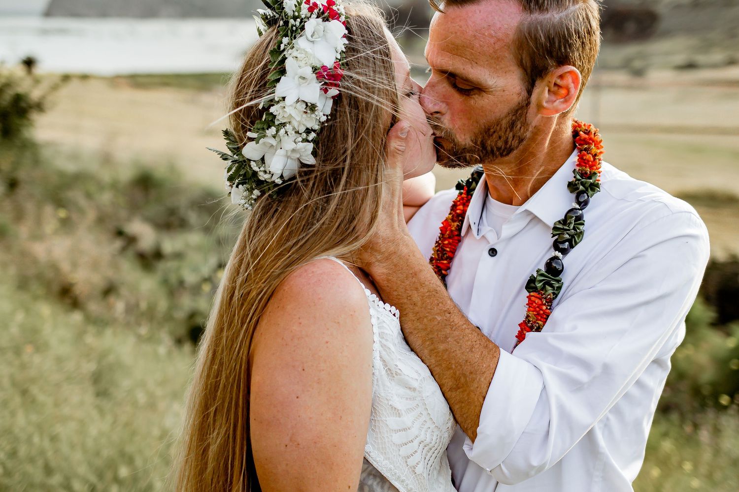 A couple shares an intimate moment at their tropical wedding, wearing traditional Hawaiian leis and a floral crown.