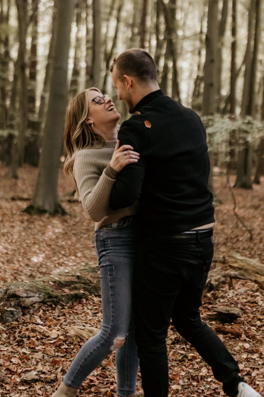 A couple laughing and dancing together on fallen autumn leaves.