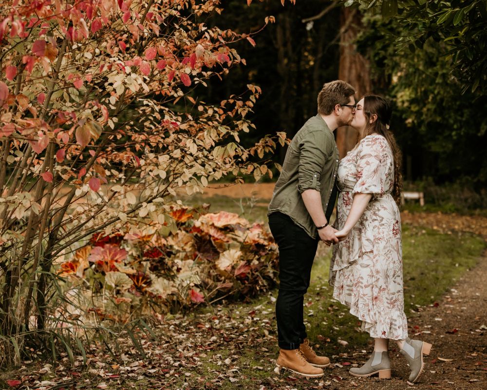 A romantic autumn portrait with red maple leaves framing a couple on a garden path.