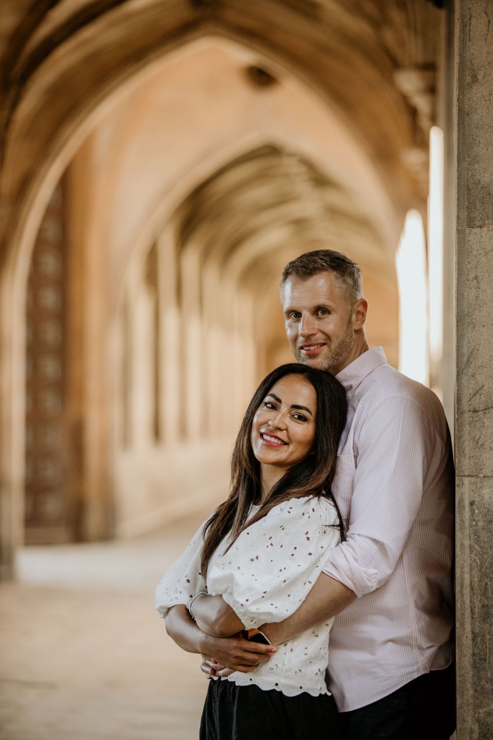 Romantic couple pose in sunlit stone archway during engagement photoshoot.