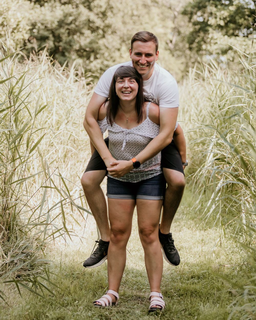 A playful couple shares a piggyback ride moment in a sunny meadow setting.