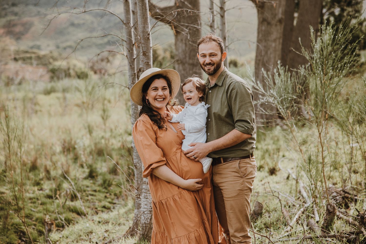 Family portrait in casual attire standing together in a wooded mountain setting.