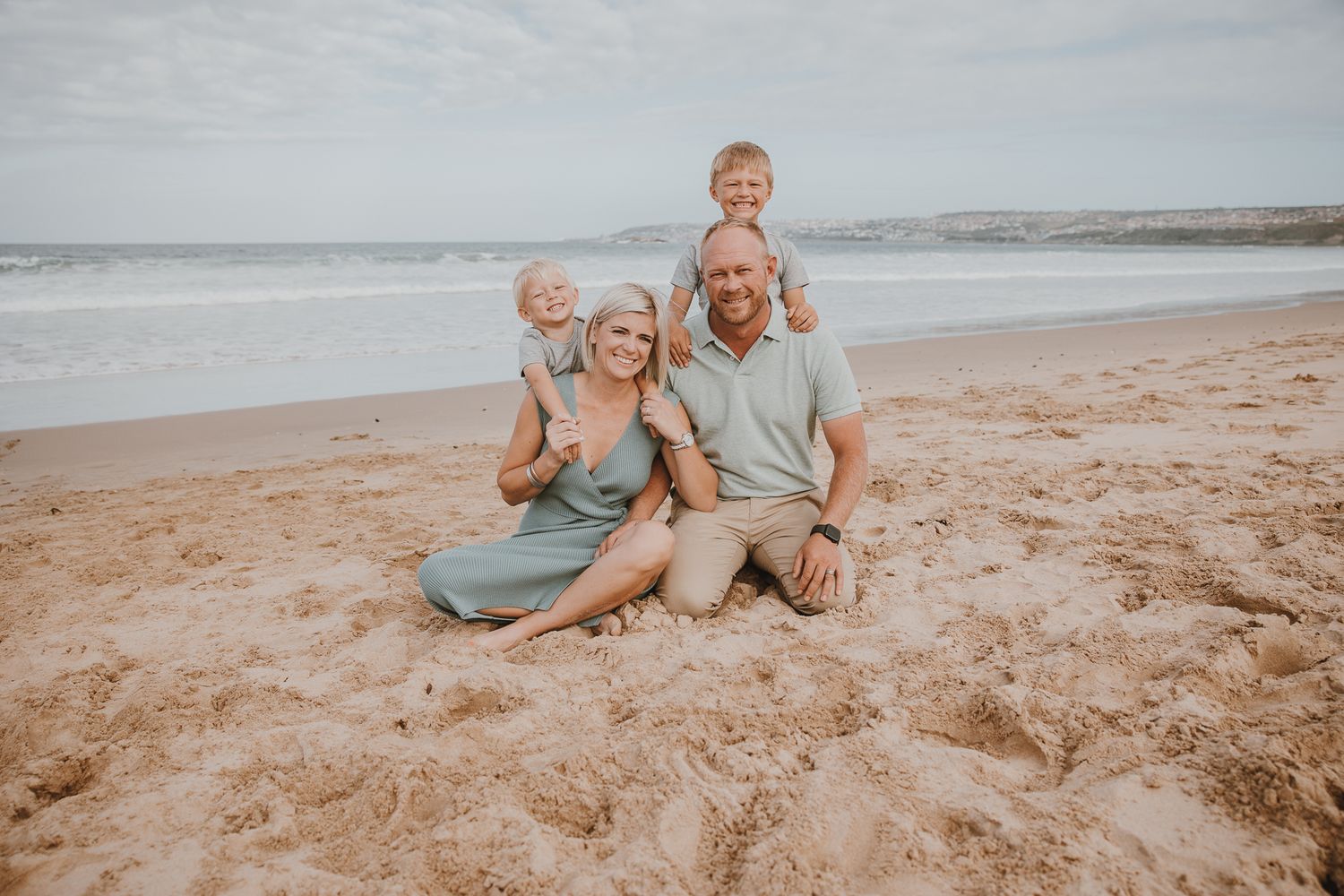 Family sitting together on a sandy beach with ocean waves in the background.