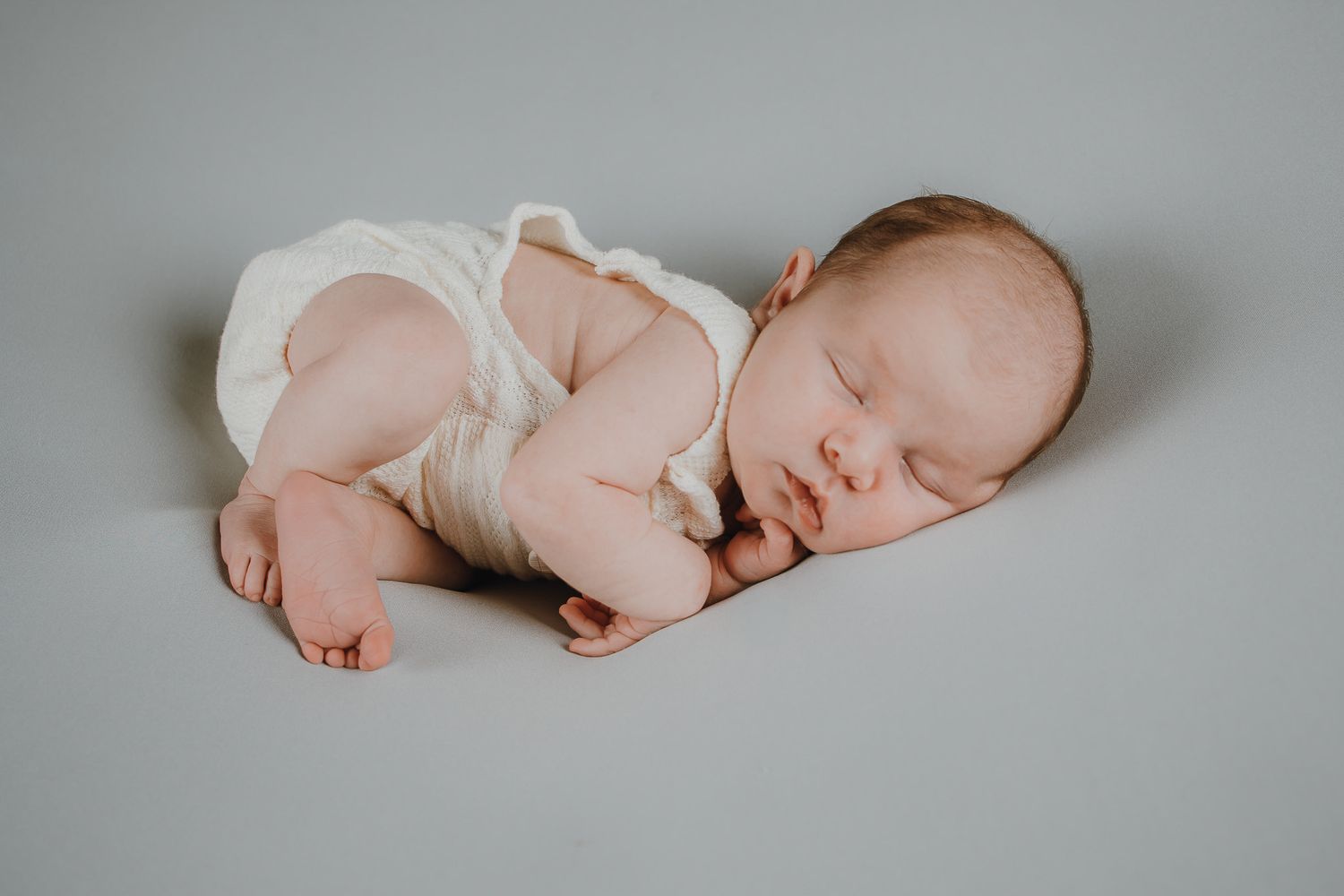 Sleeping newborn baby wearing white onesie on gray background.