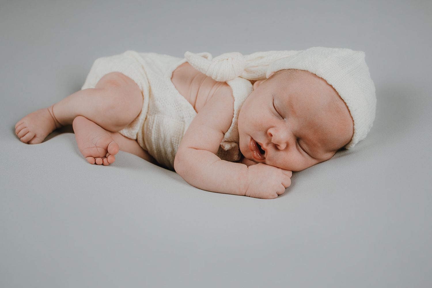 Sleeping baby wrapped in white blanket lying on grey background.