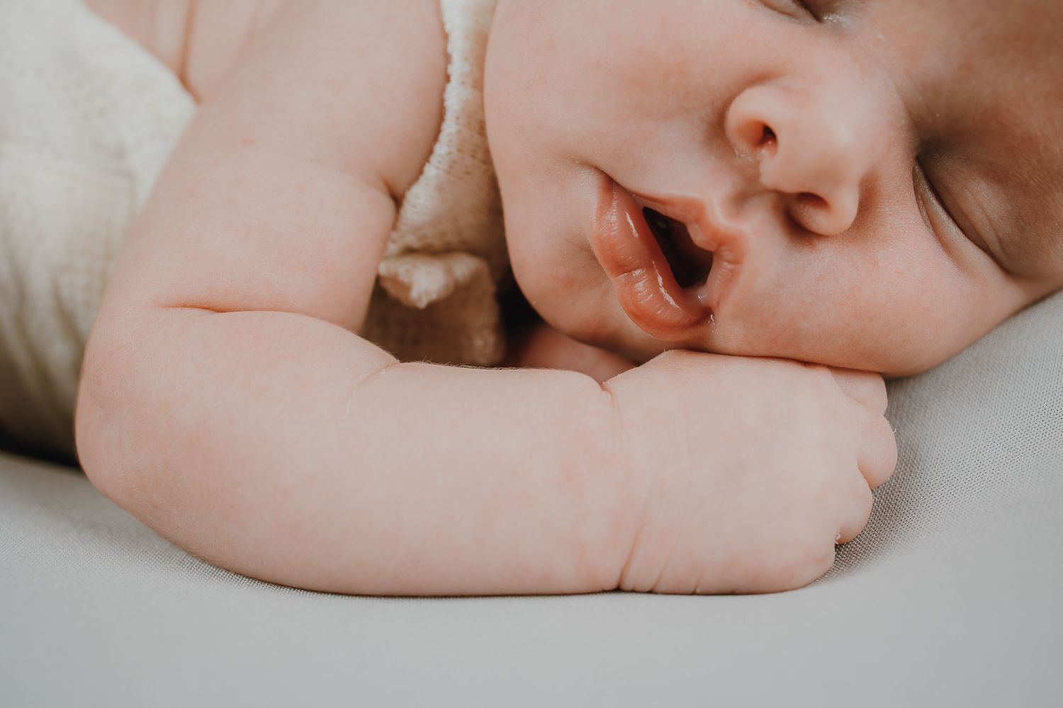 Close-up of sleeping baby's face with tiny hand near mouth.