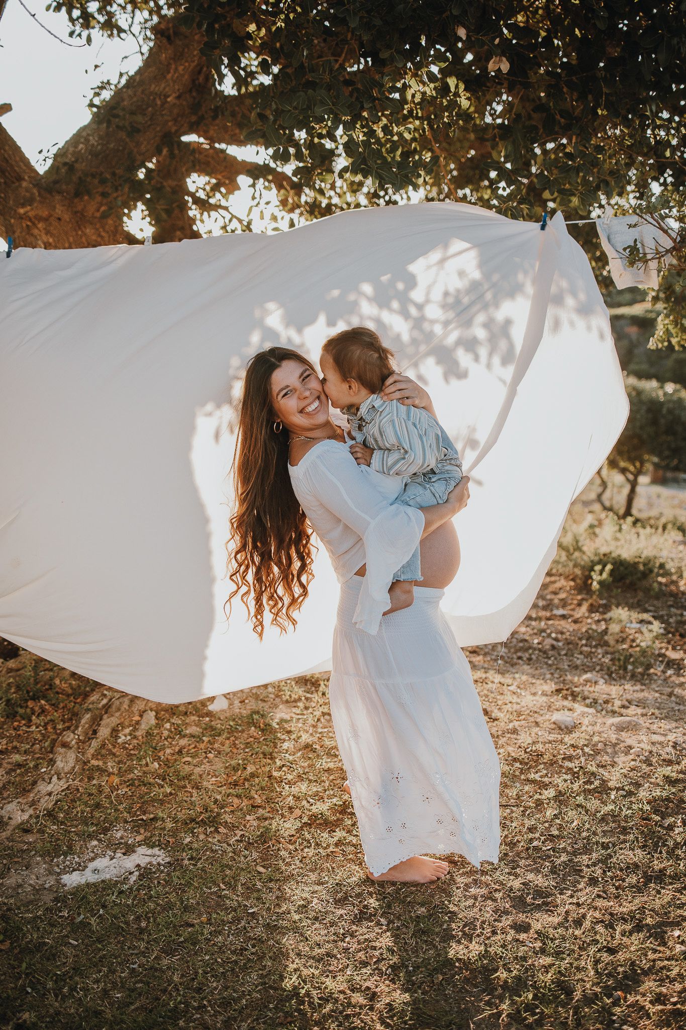 Mother and child sharing a tender moment against billowing white fabric outdoors.