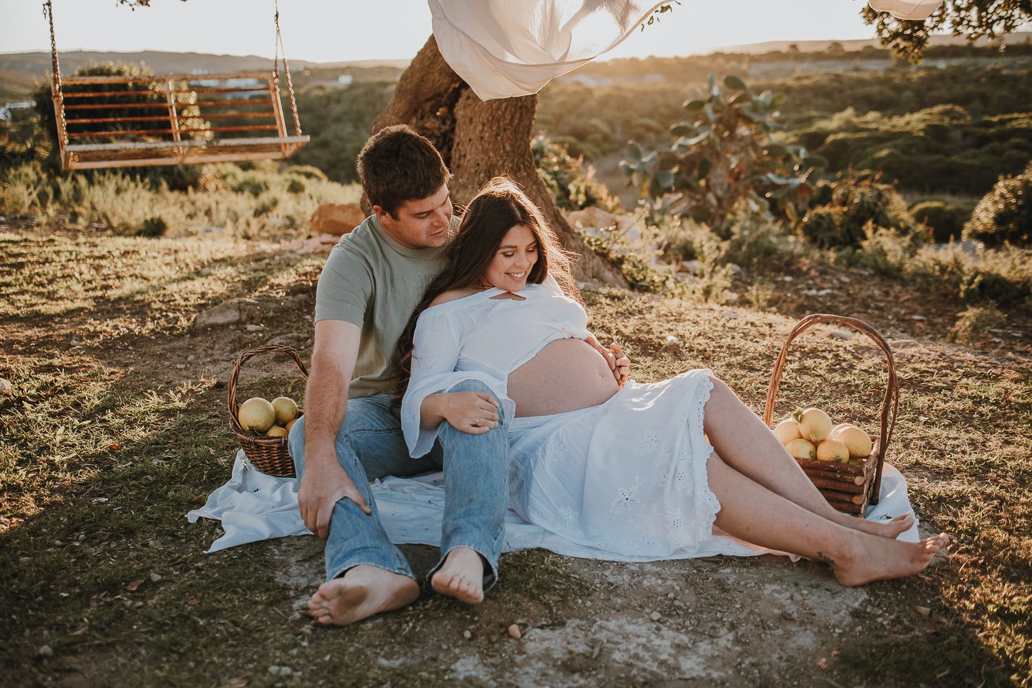 Couple relaxing on blanket during sunset maternity photoshoot.
