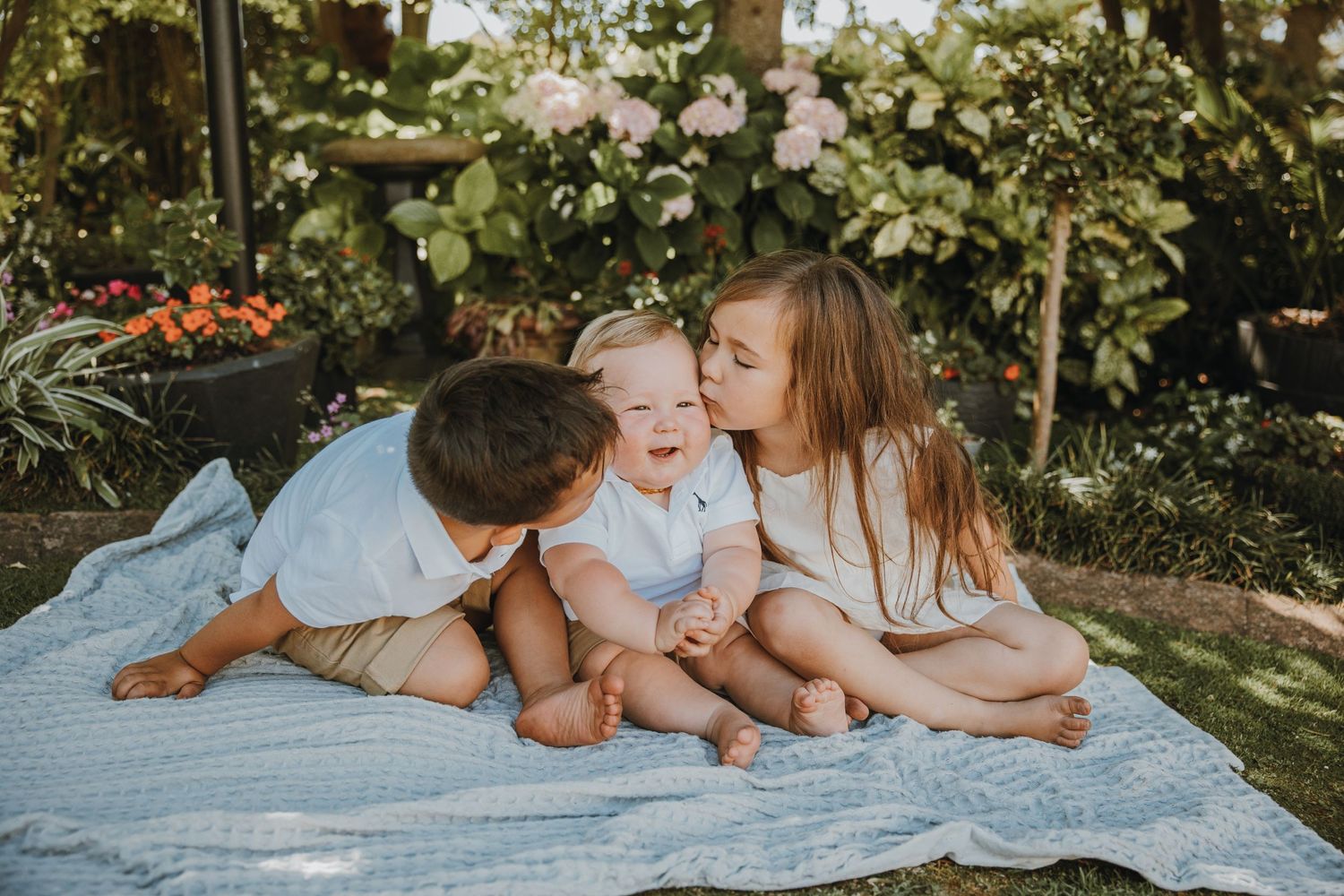 A family shares a tender moment while relaxing on a blanket in a garden setting.