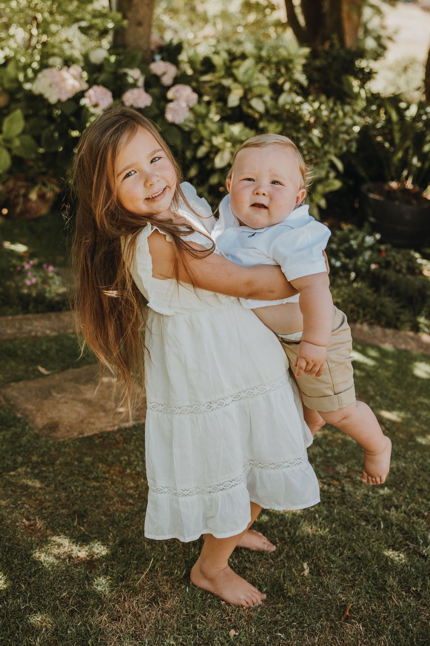 Two siblings share a joyful moment together in a garden setting.