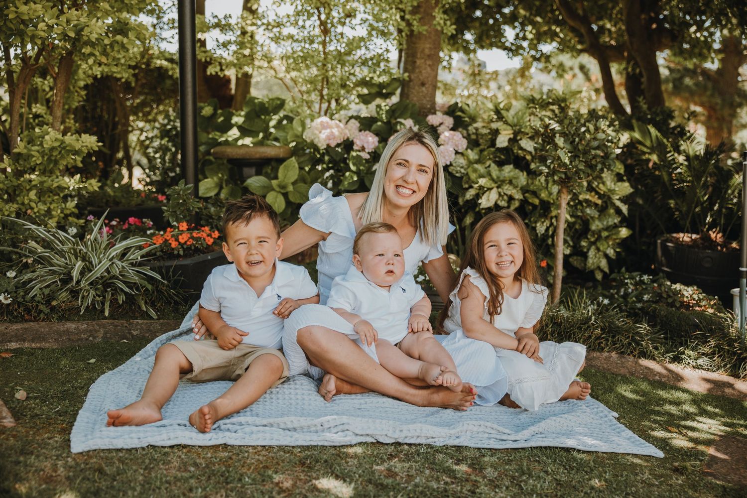 A group sits together on a picnic blanket in a sunny garden.