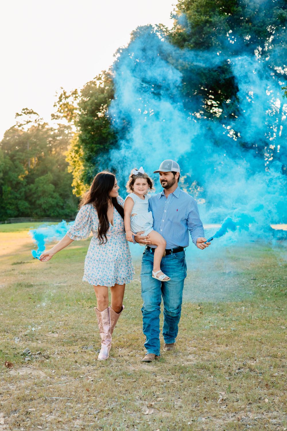 Family portrait outdoors with vibrant blue smoke bomb creating a magical effect in nature.