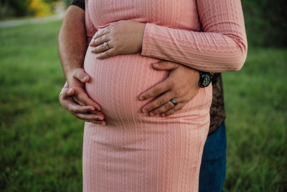 Close up of hands cradling a pregnant belly in pink sweater outdoors.