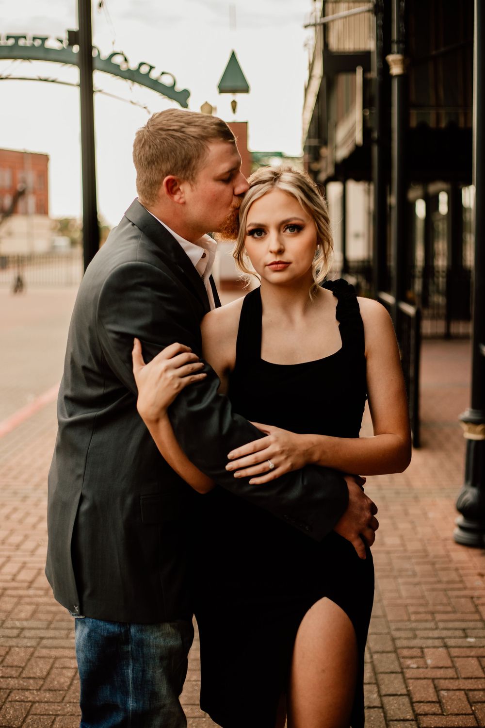 Romantic couple embracing on brick street with historic architecture in background.