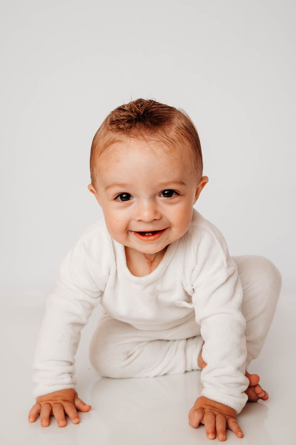 Happy baby in white onesie crawling on white background.