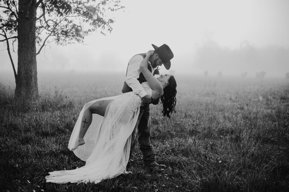 A romantic black and white photo shows a couple in wedding attire sharing an intimate moment outdoors.
