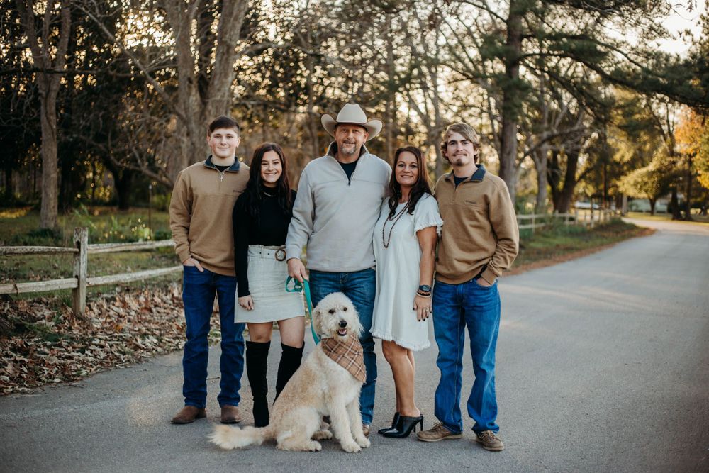 A casual outdoor group portrait with a goldendoodle dog on a tree-lined path during autumn.