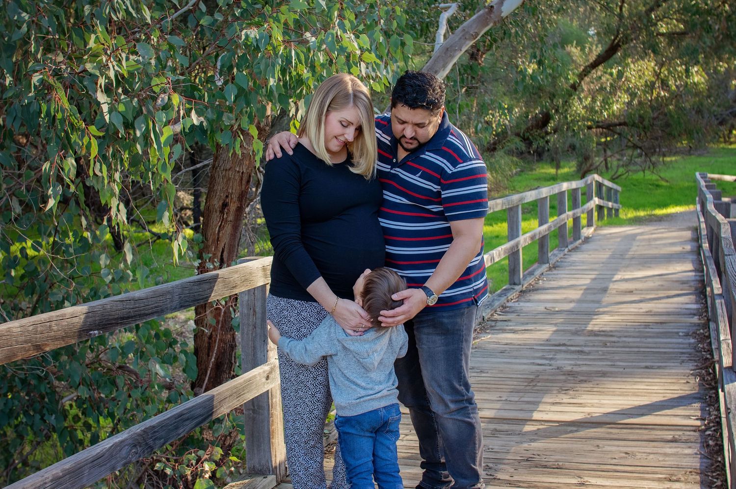 family embracing outside, toddler looking at mums pregnant belly