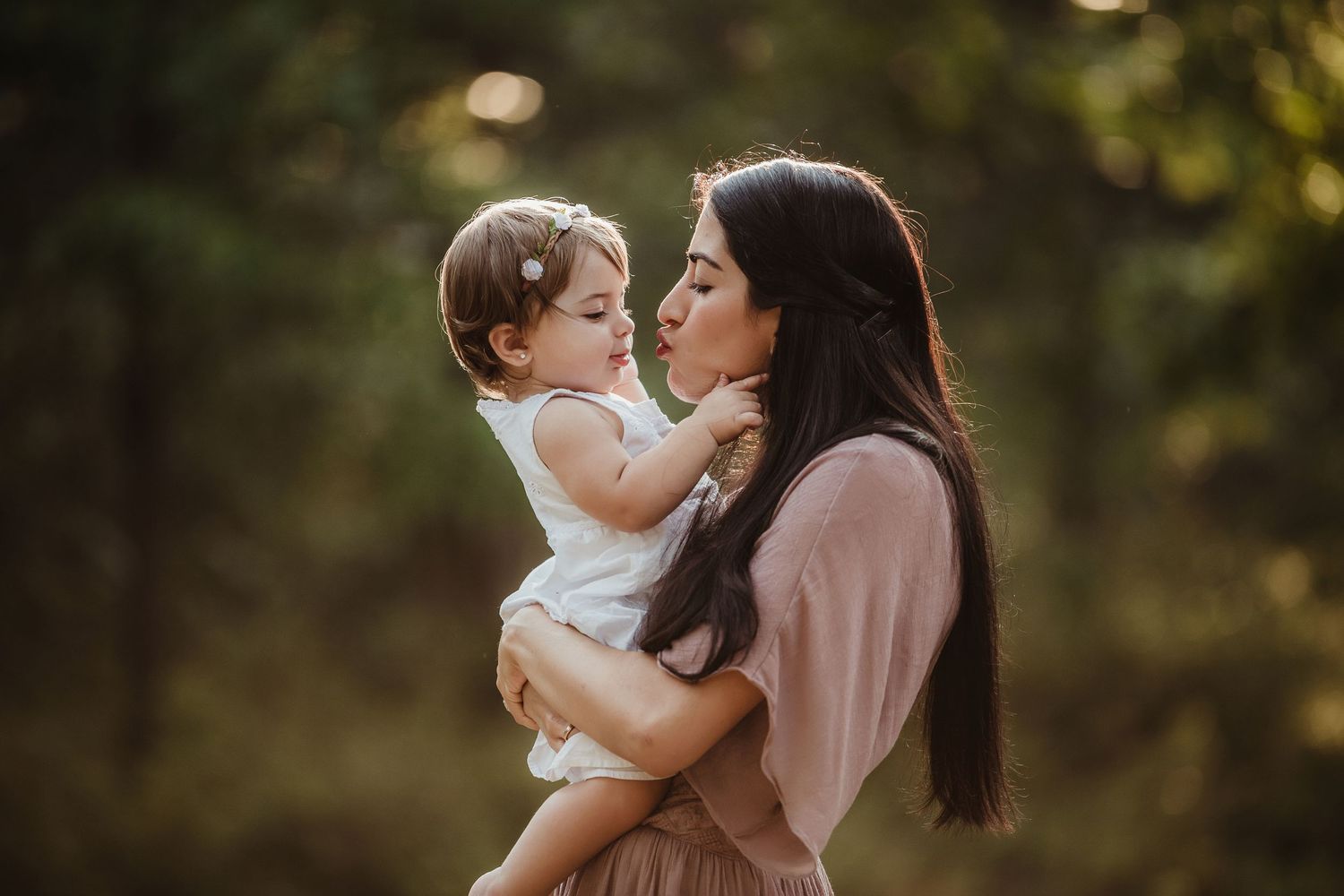 Tender outdoor portrait of parent and child embracing in soft natural lighting.