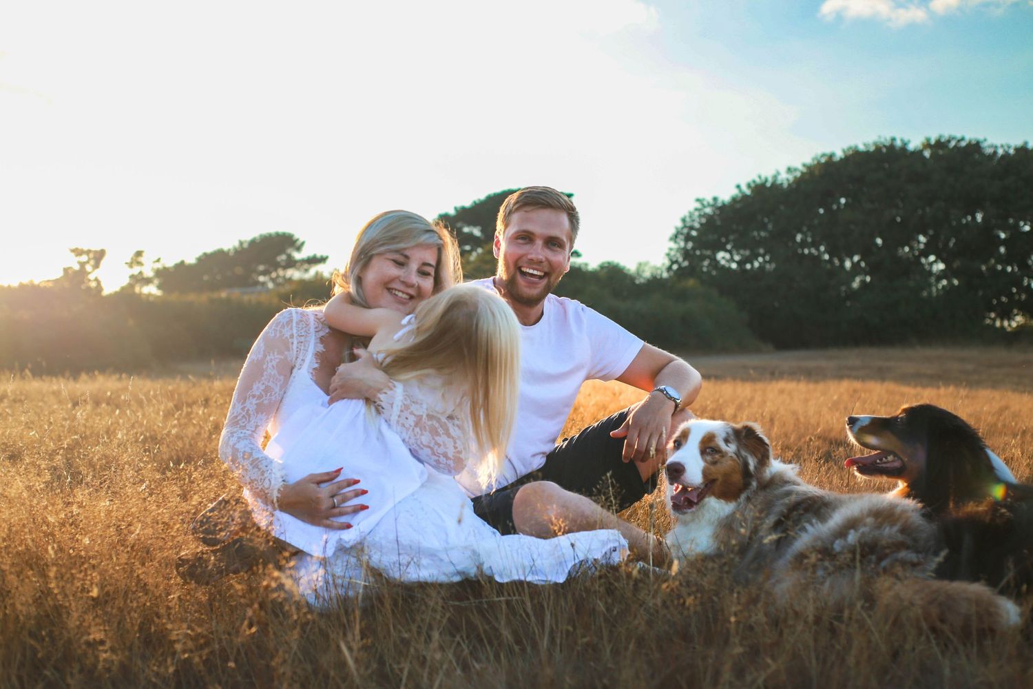 Family and dog relaxing together in sunny wheat field during golden hour.