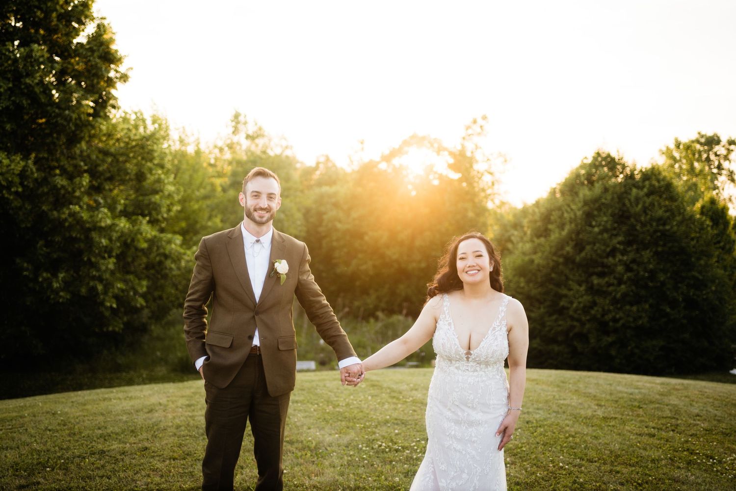 Newlyweds hold hands and laugh together in an outdoor sunset portrait.