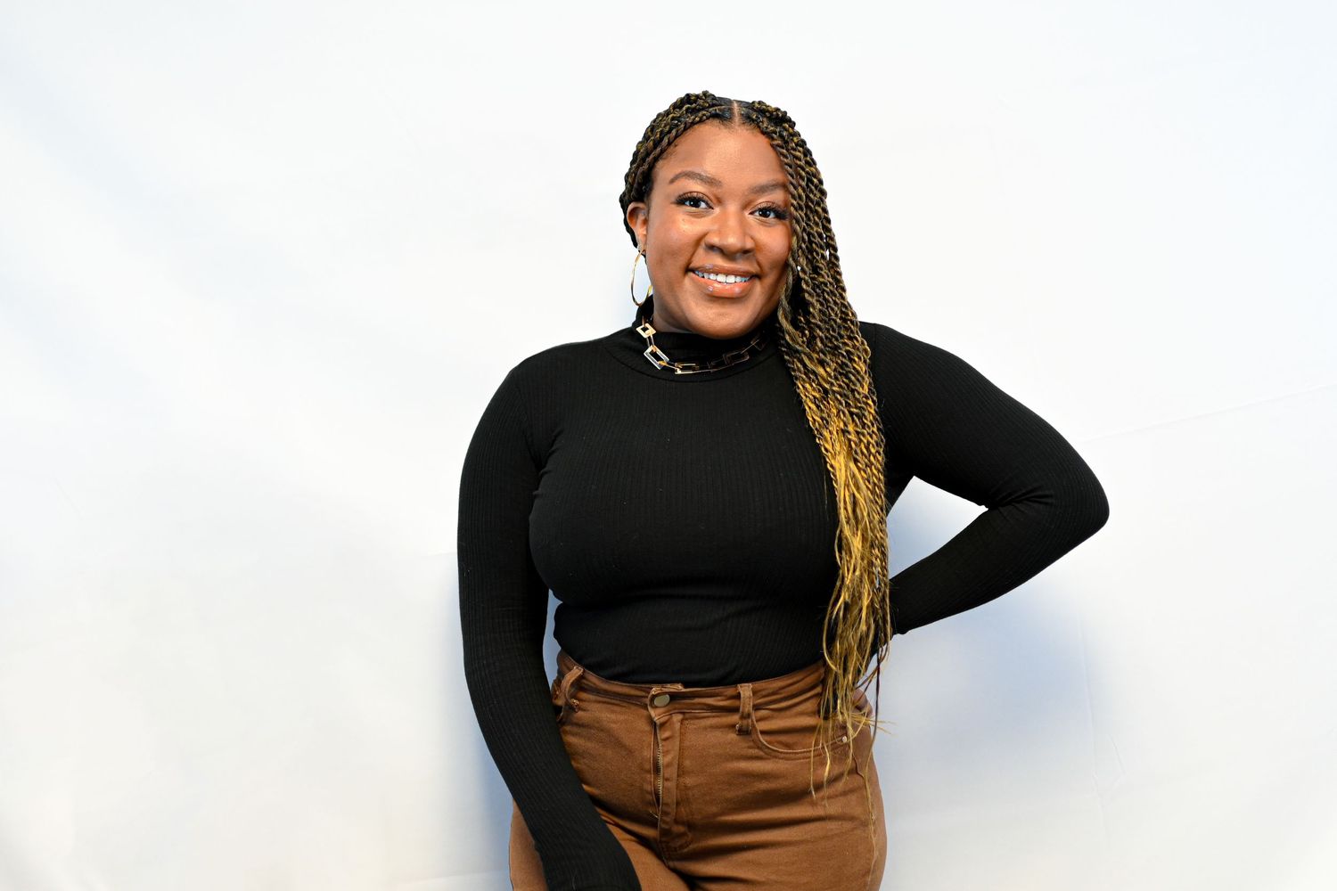 Portrait against white background featuring brown pants and black top with braided hairstyle.