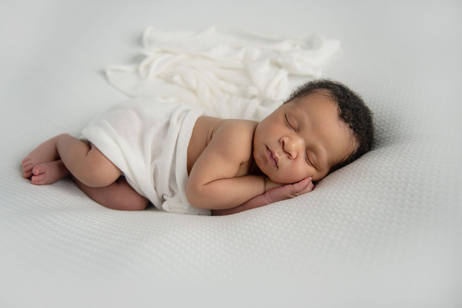 A peaceful newborn photo shoot with soft white bedding and gentle natural lighting.