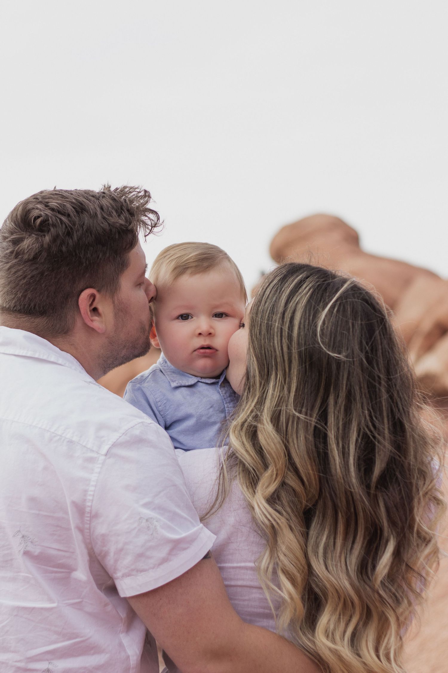 Family in white and light blue outfits sharing a tender moment together against a light background. family photoshoot, Colorado Springs