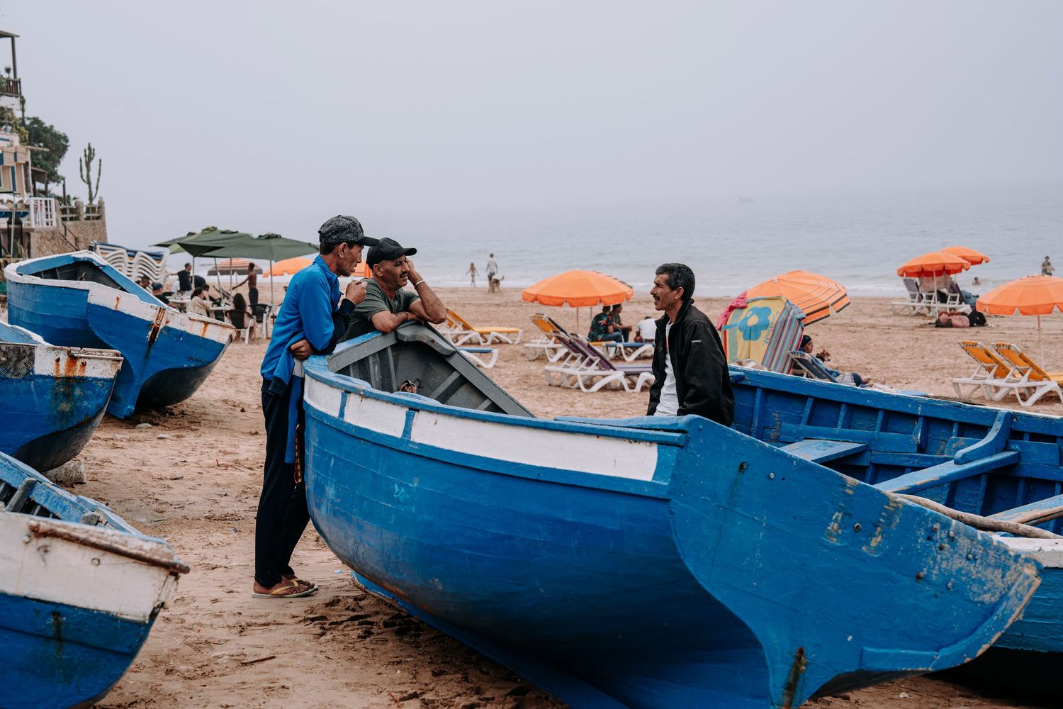 Two people working with traditional blue fishing boats on coastal beach.