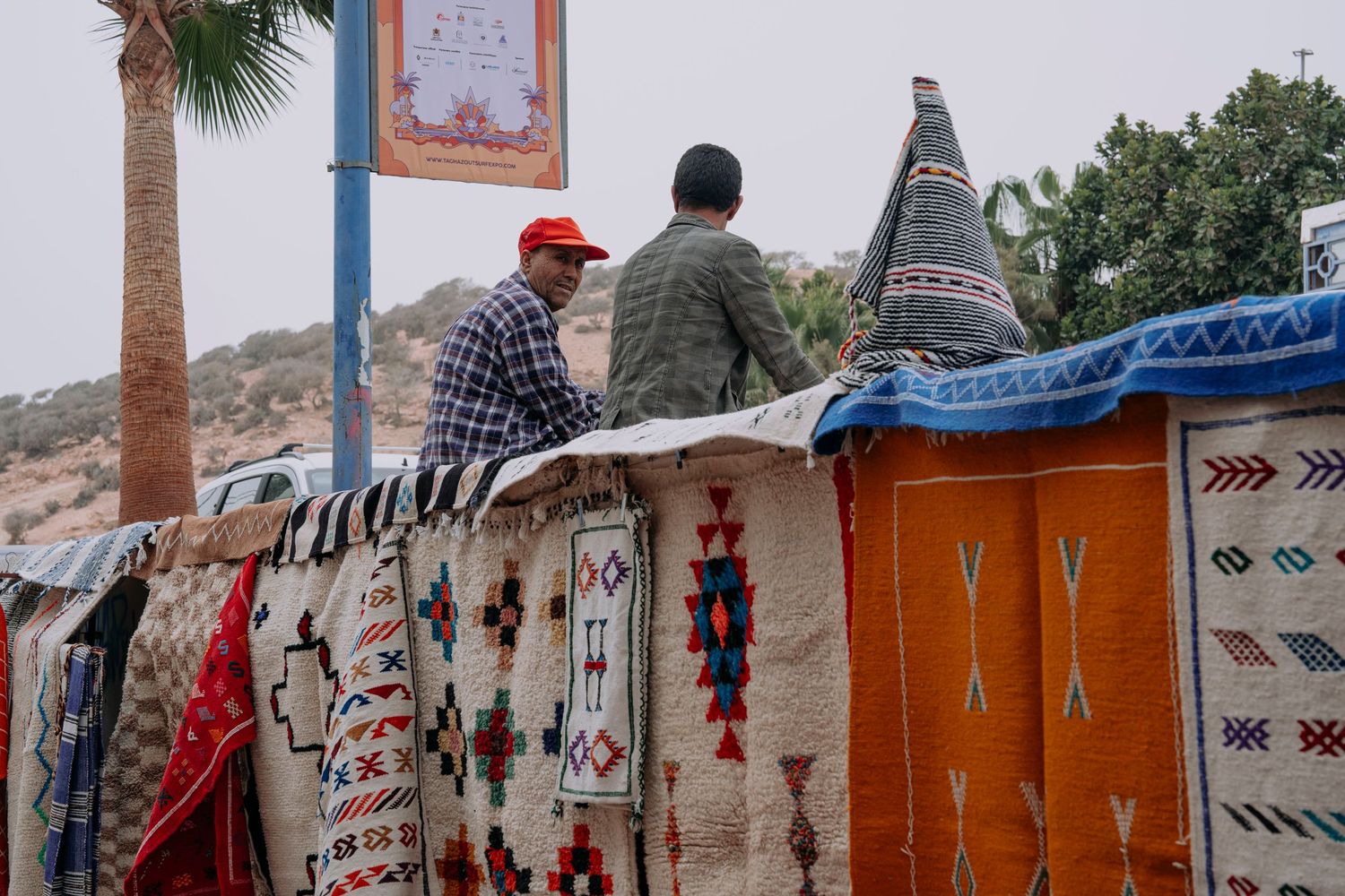 Colorful traditional rugs and textiles displayed at an outdoor market with geometric patterns and designs.