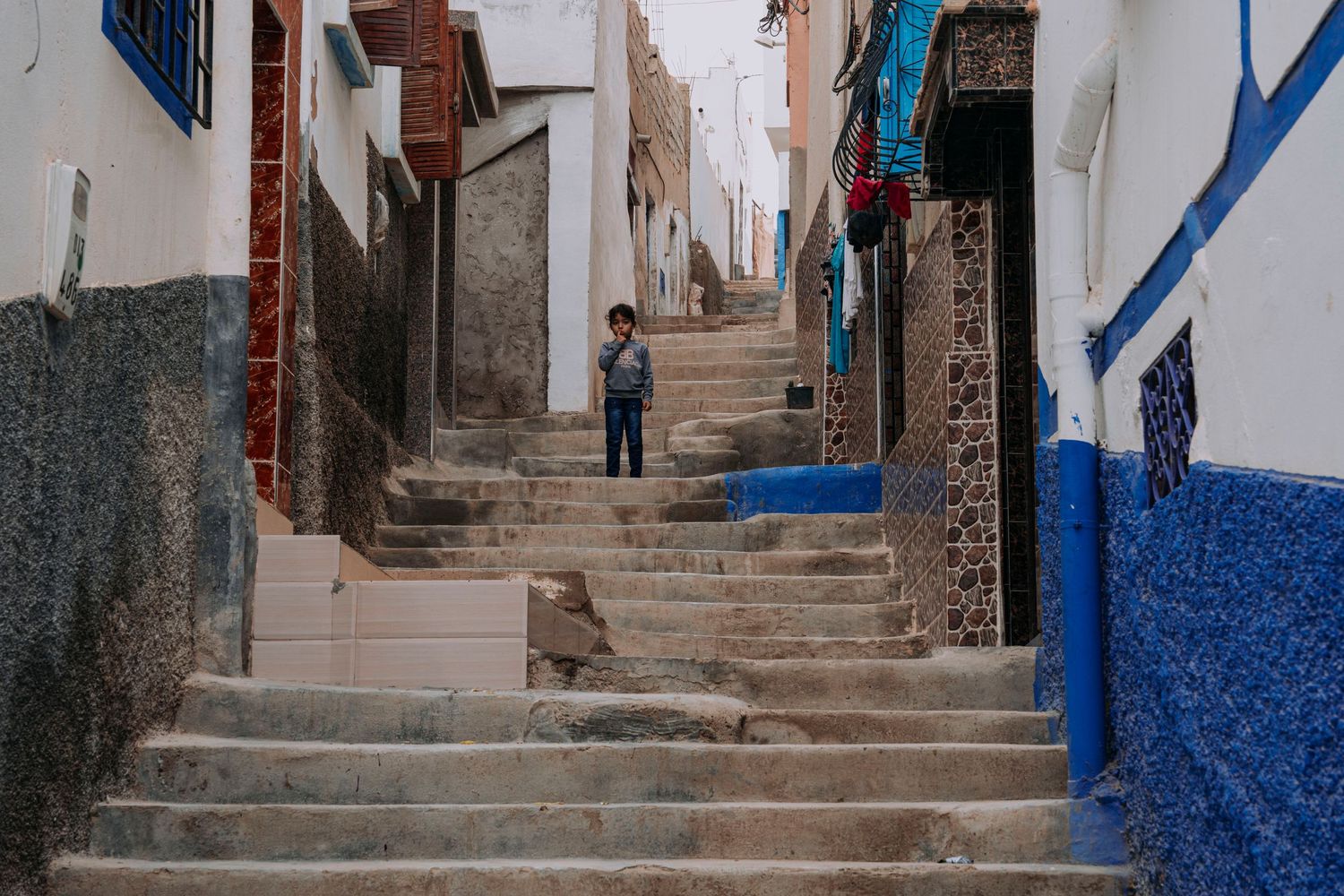 Narrow alleyway with white and blue painted walls leading up stone steps in a Mediterranean town.