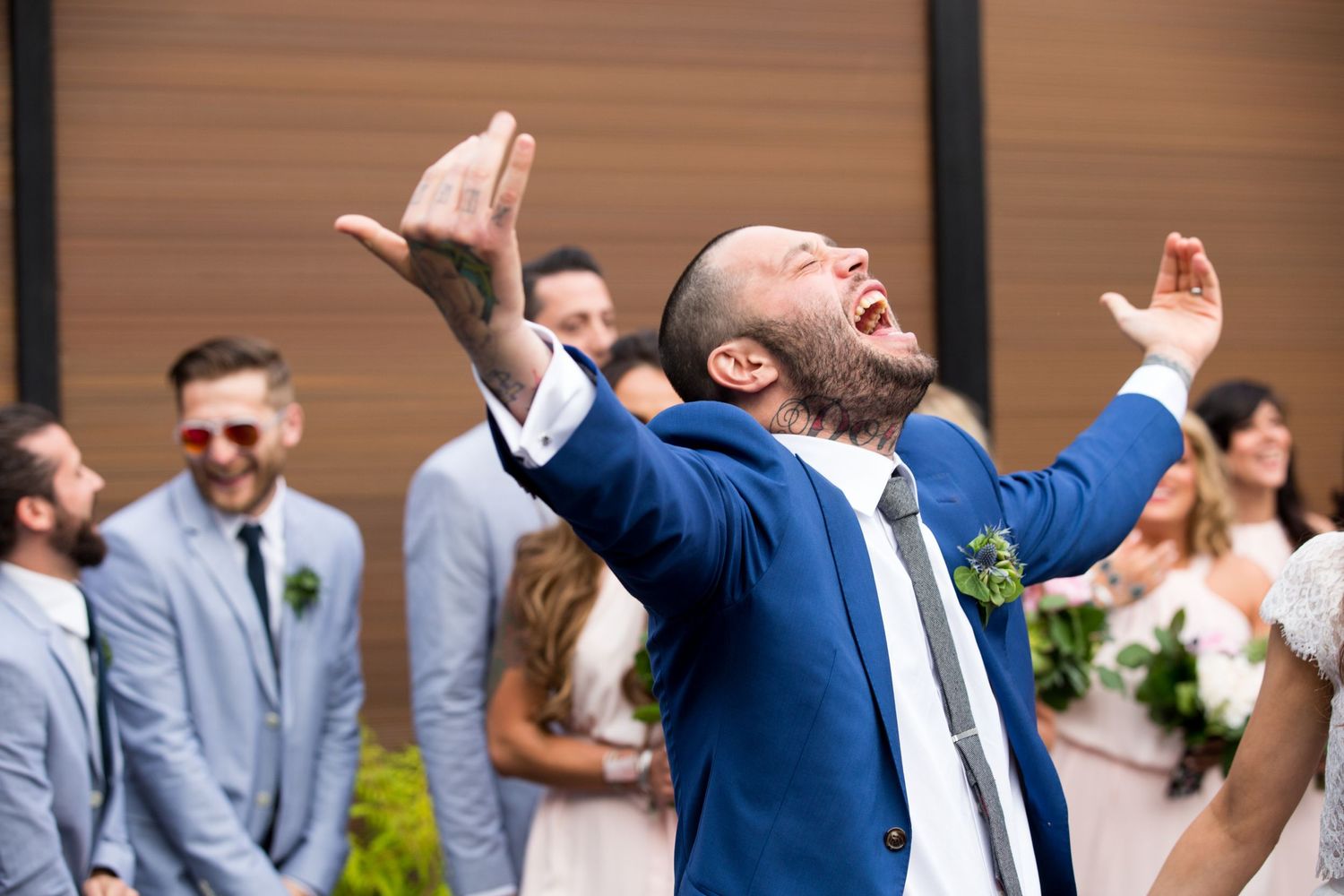 Wedding guest in blue suit celebrating joyfully during outdoor ceremony.