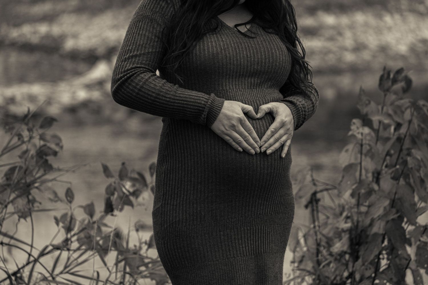 Vintage style maternity photo with hands forming heart shape over pregnant belly.