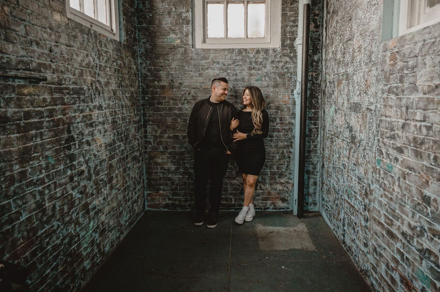 Intimate couple photoshoot in an industrial brick-walled corridor with window light.