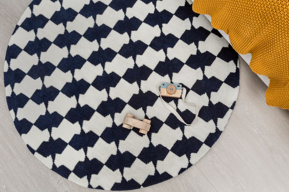 Round navy and white checkered play mat with wooden toy cars on light floor.